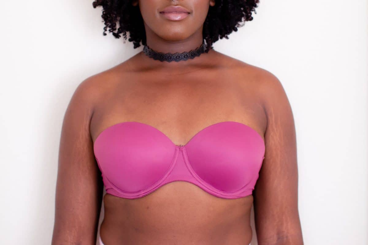 A woman with curly hair wearing a pink strapless underwire bra and a black choker