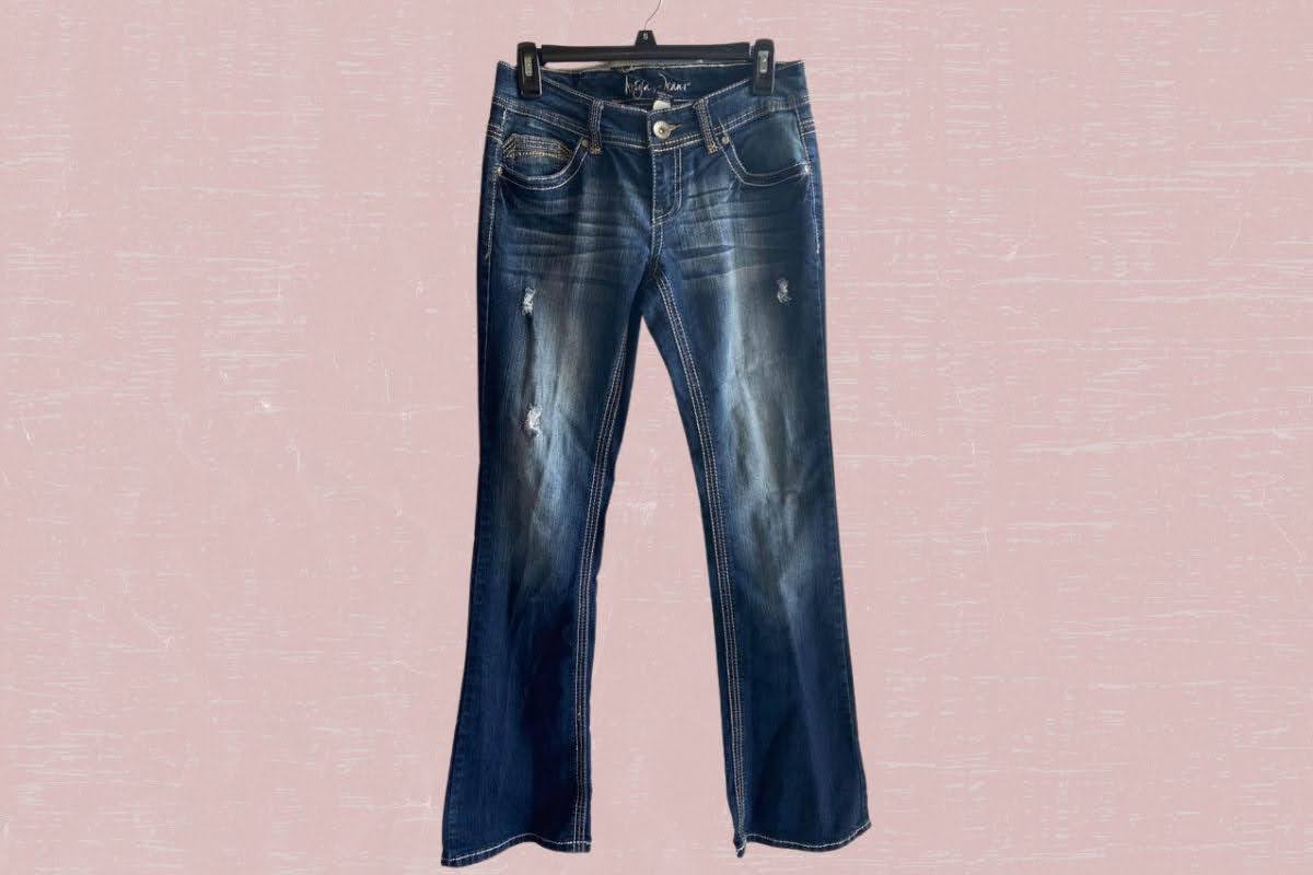 Blue denim jeans with pockets hang on a black hanger placed on a pink background