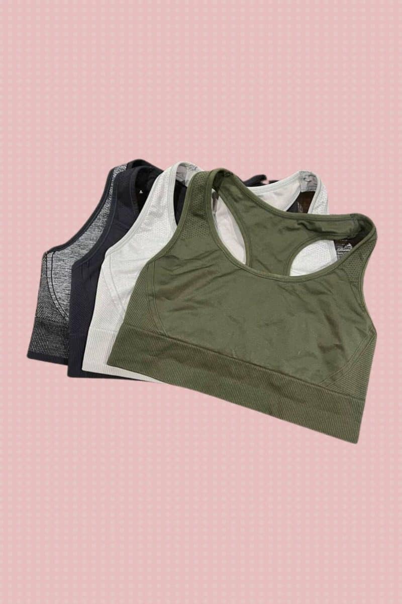 Four different colors of seamless sports bras are placed on a pink background