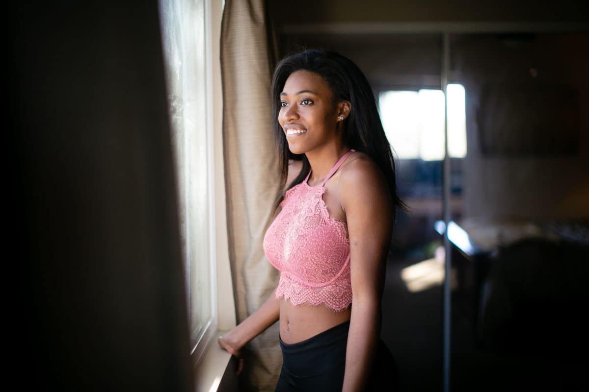 A woman wearing a pink lace wired longline bra and black leggings looking at the window