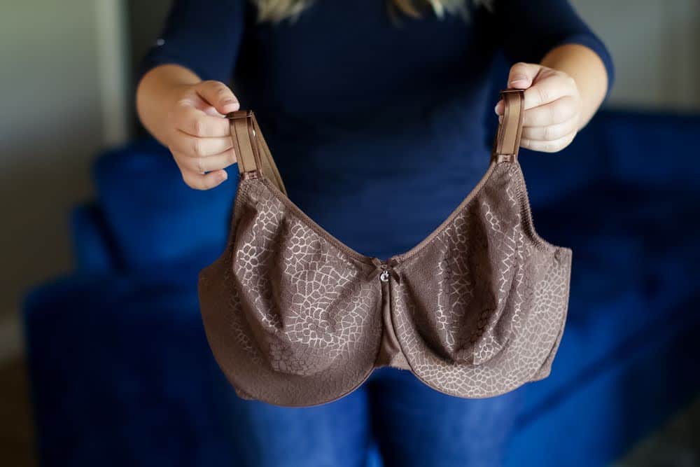 A woman holding a brown minimizer bra with adjustable and wide straps