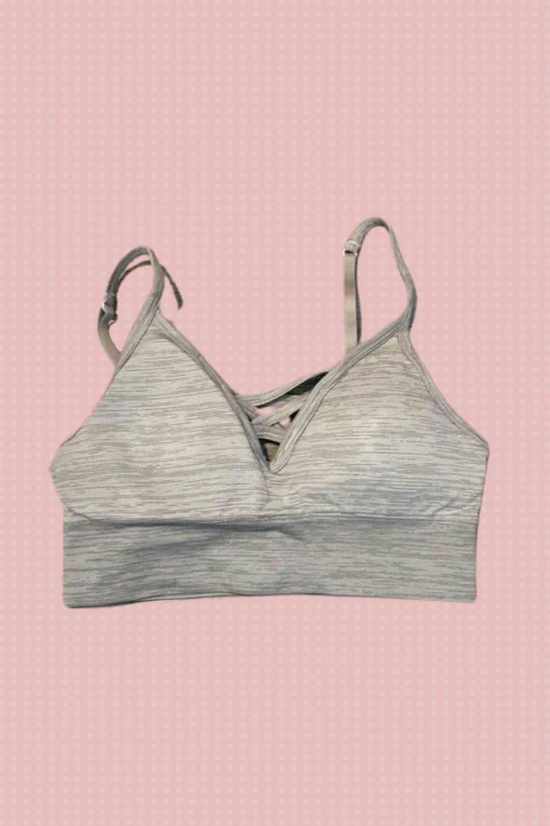 Gray sports bra with adjustable straps and wide band placed on a pink background