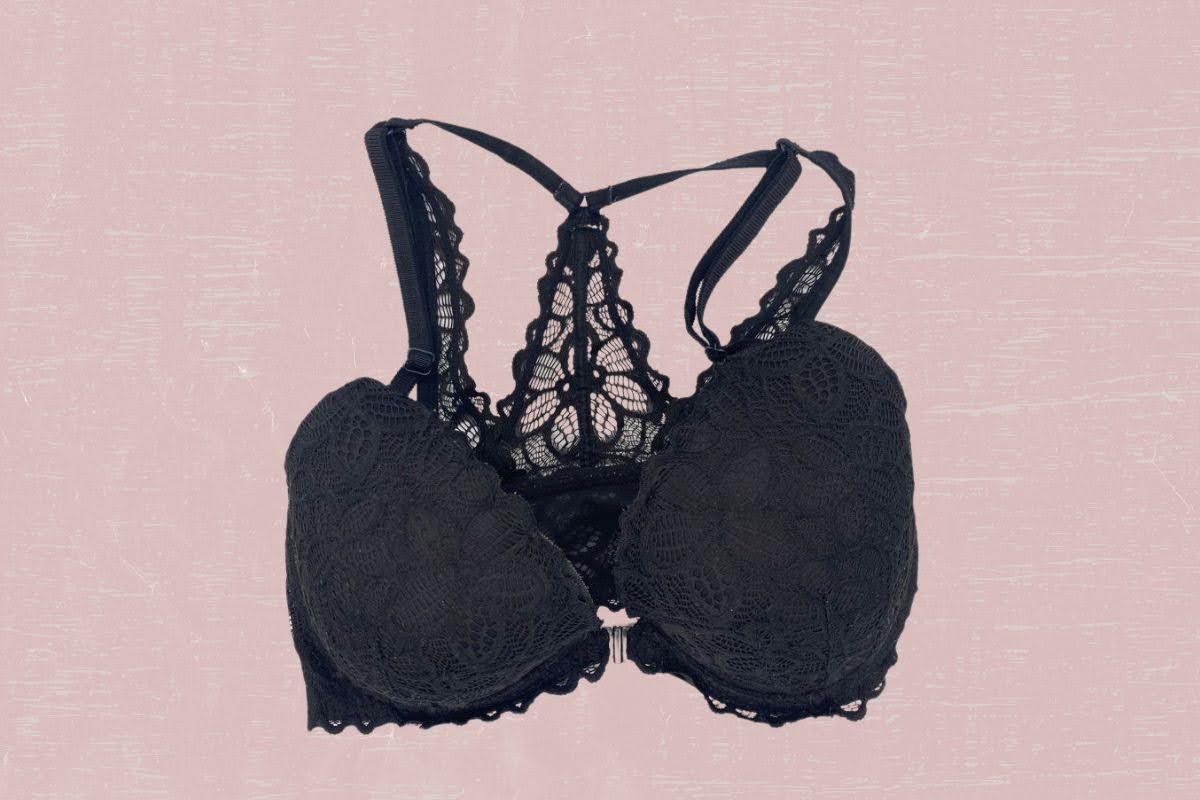 A black halter bra with front clasps and floral lace design is placed on pink background
