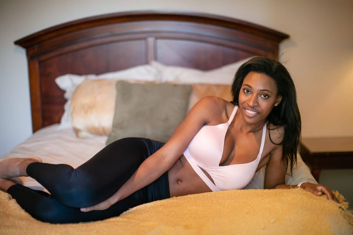 A woman wearing a white wireless racerback bra and black leggings while lying in bed