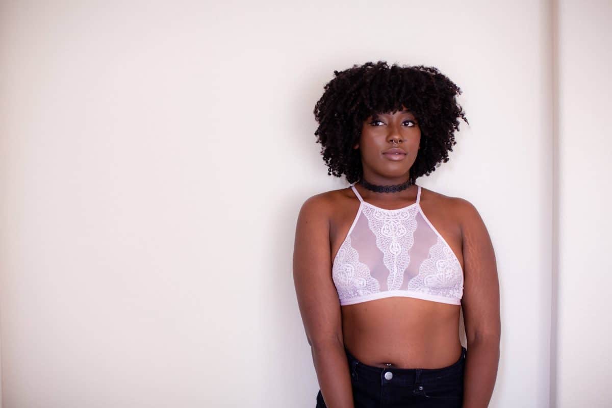 A woman wearing a white high-neck bralette and black jeans standing near a white wall
