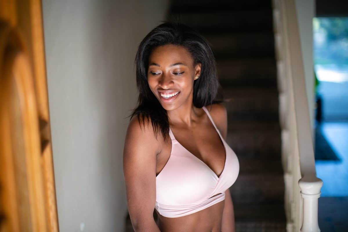 A woman wearing a white full-coverage padded bra with adjustable straps is standing near a staircase