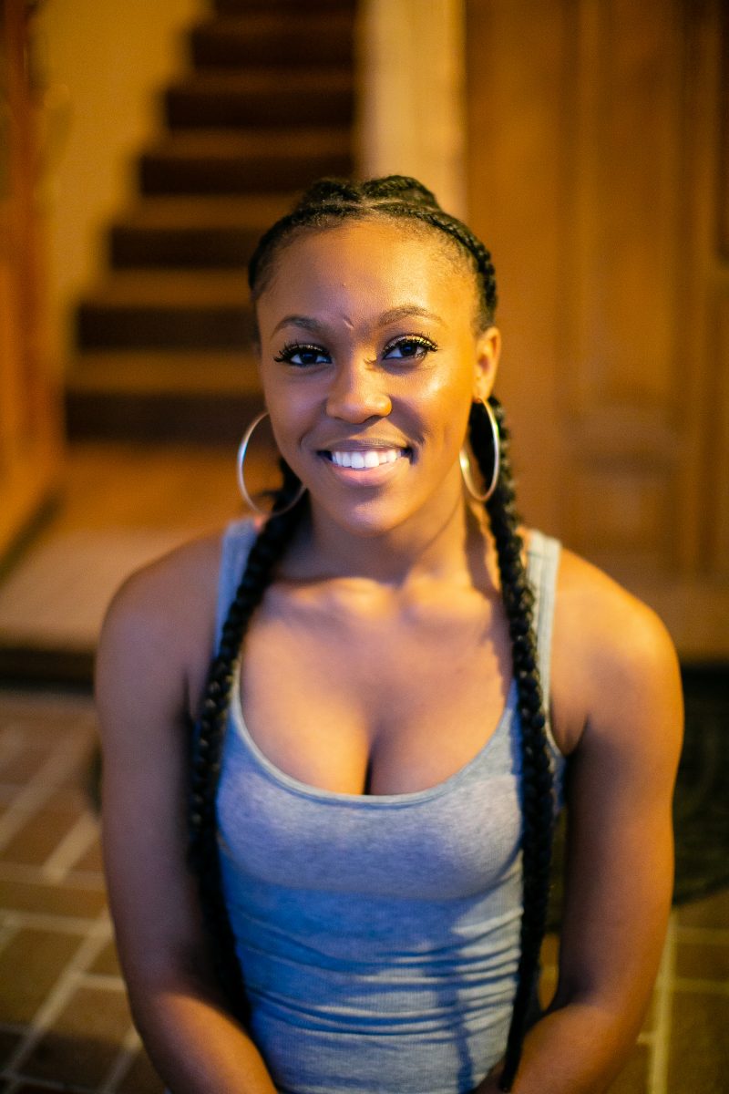 A woman with braided hair wearing a gray tank top and silver hoop earrings