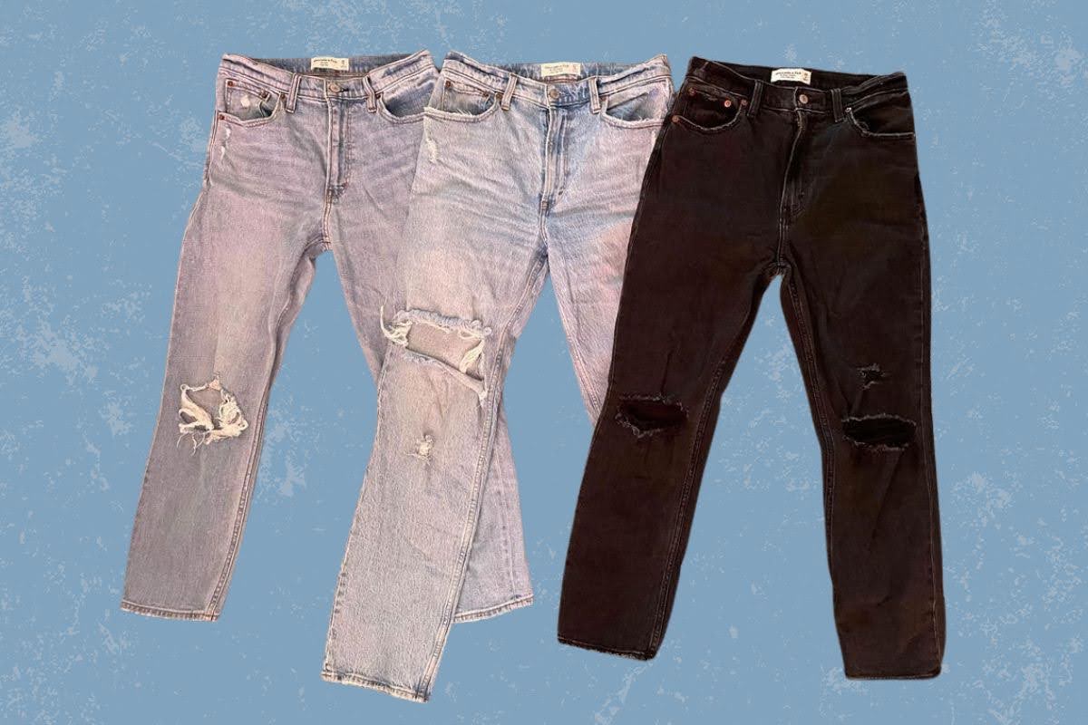 Three different colors of tattered denim jeans are placed on a blue background