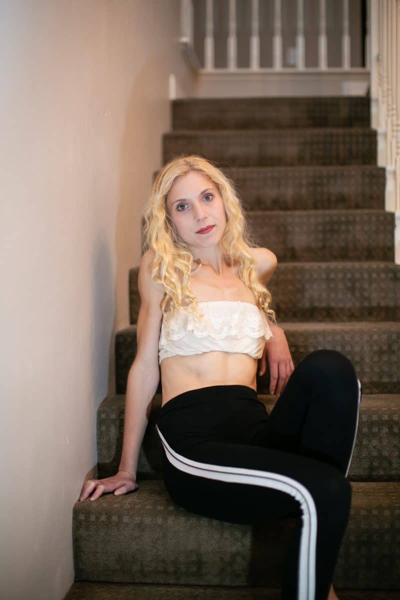 A woman wearing a bandeau lace bralette and black leggings seated on the stairs