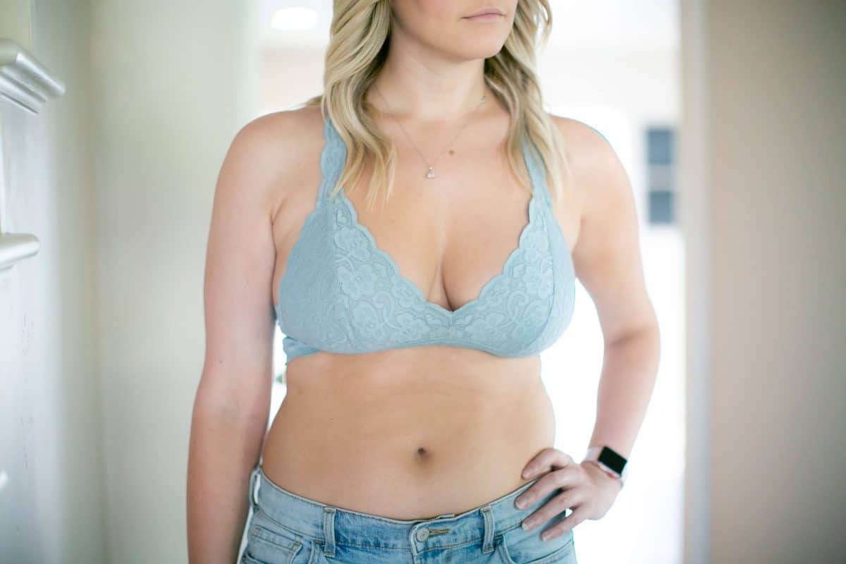 A woman in blue lace bralette and denim shorts wearing a smartwatch and a necklace
