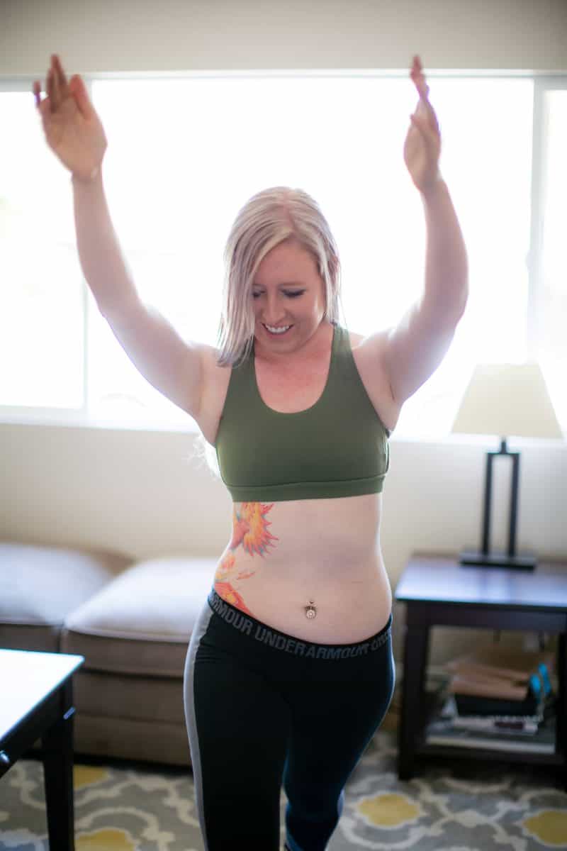 A woman in a green sports bra and black leggings is exercising in the living room