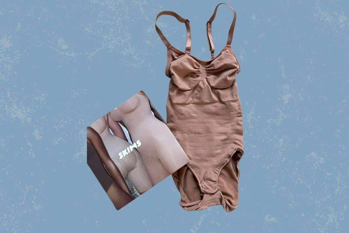 A brown full-body shapewear with wide and adjustable straps placed on a blue background