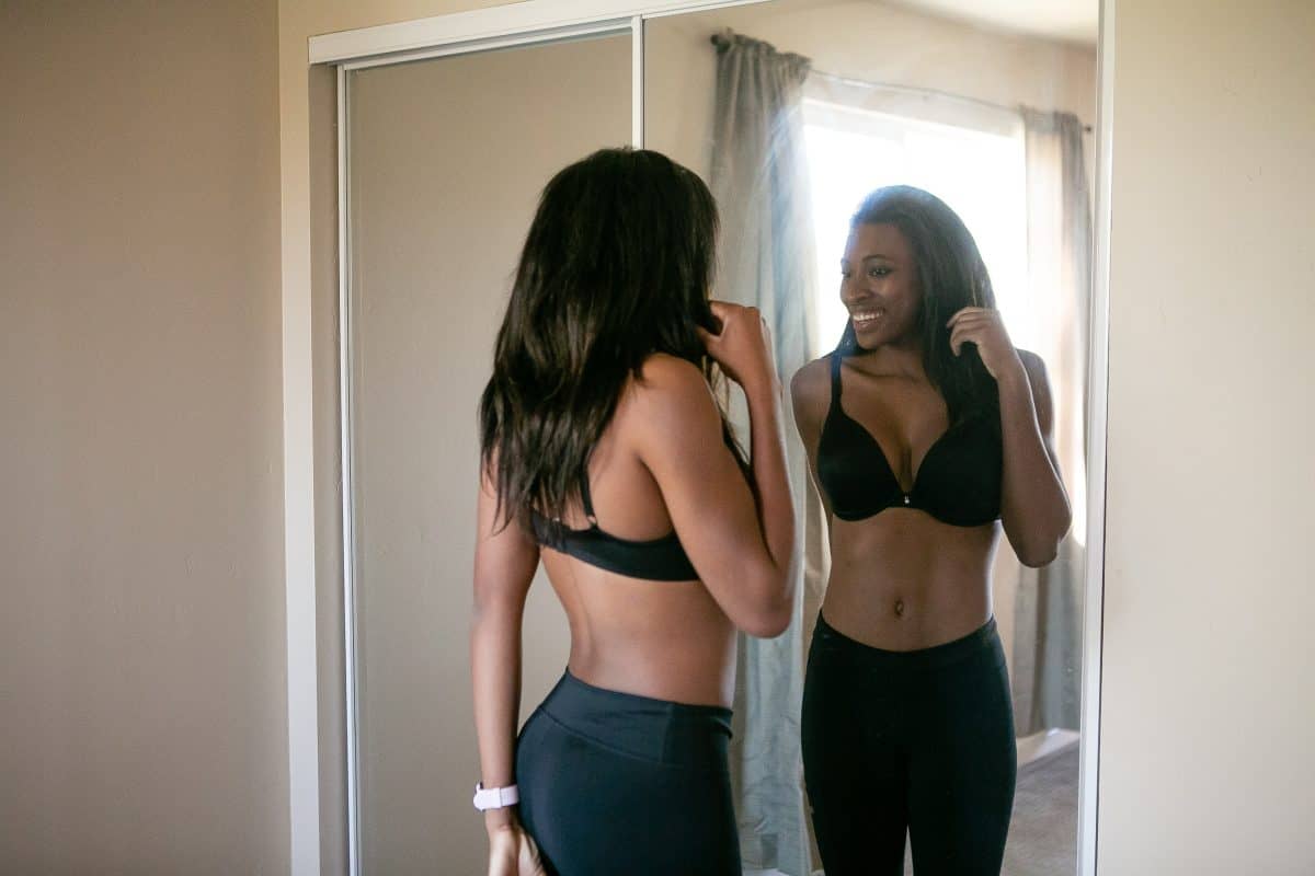 A woman looking in the mirror wearing a black push-up bra and black leggings