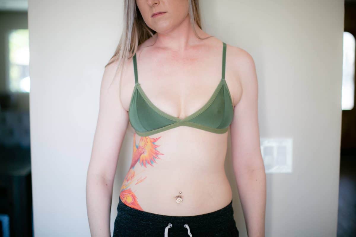 A woman wearing a green unpadded bra and black jogging pants standing near a white wall