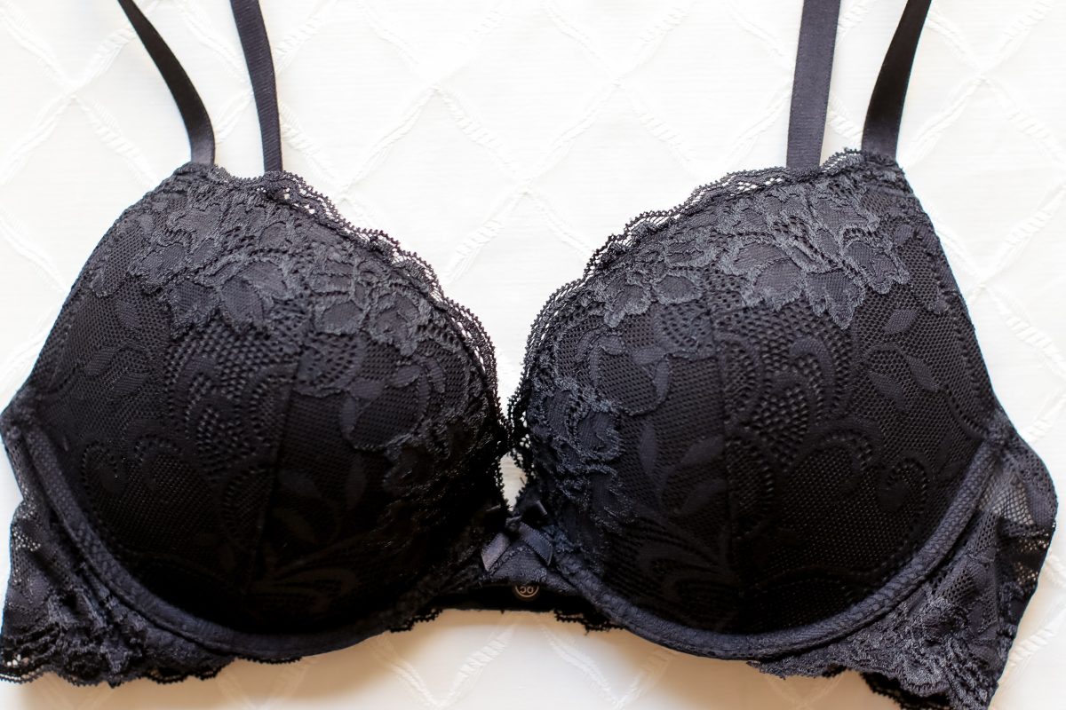 A black plunge bra with a floral lace design and an underwire placed on a white surface