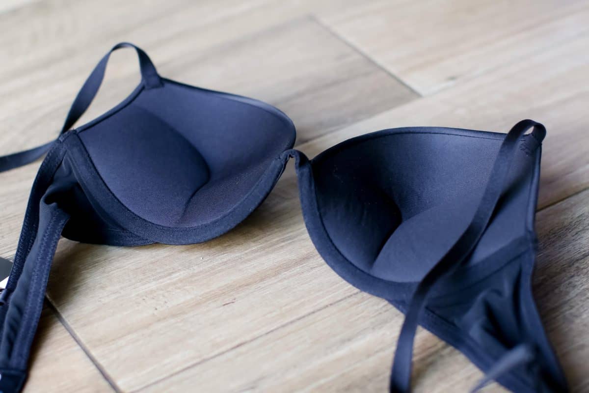 A back view of a black padded bra with underwire and adjustable straps placed on ceramic tiles