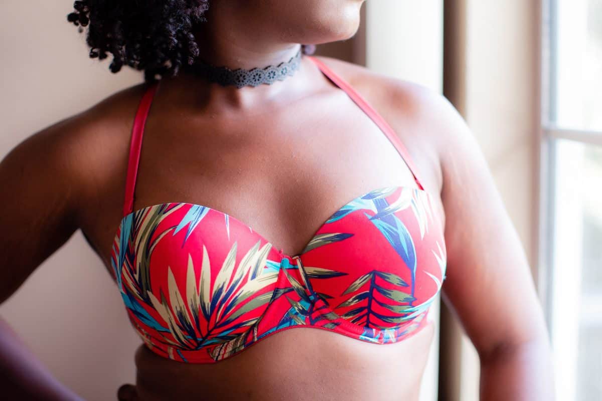 A pink halter underwired bra with a tropical design is worn by a woman standing near a window