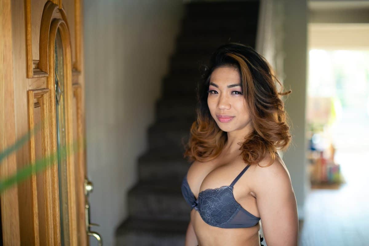 Woman wearing a gray underwire bra with adjustable straps standing near a brown door