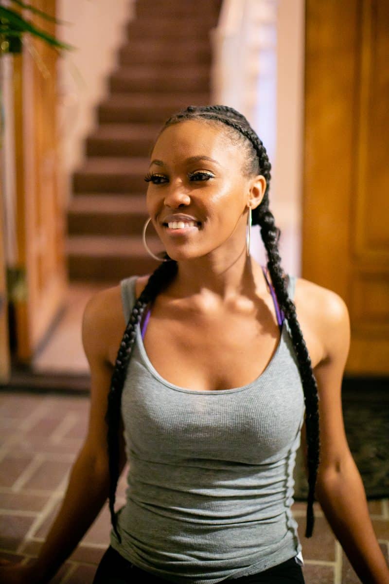 A woman in a gray tank top and black shorts seated on the ceramic tiles outside the house