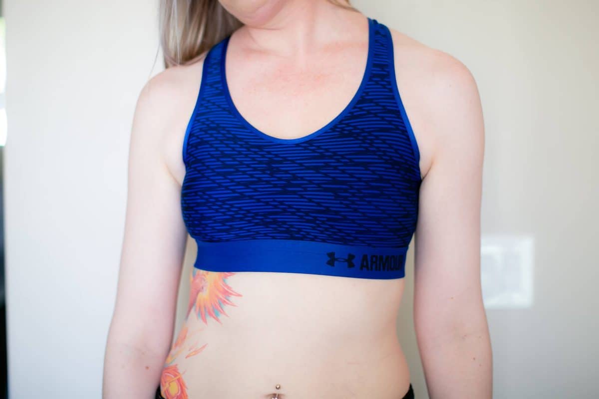 A blue Under Armour sports bra worn by a woman standing near a white wall