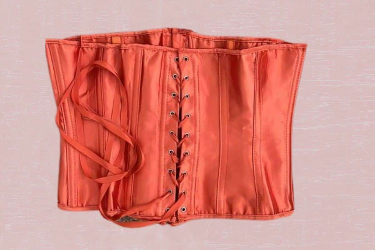 A back view of an orange corset with strings placed on a pink background