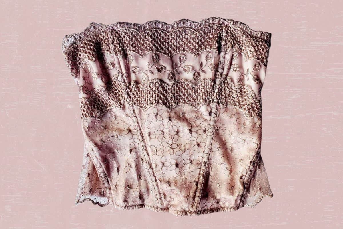 A pink corset with a floral lace design placed on a pink background