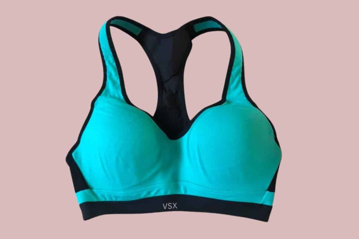 A green and black Victoria's Secret racerback sports bra placed on a pink background