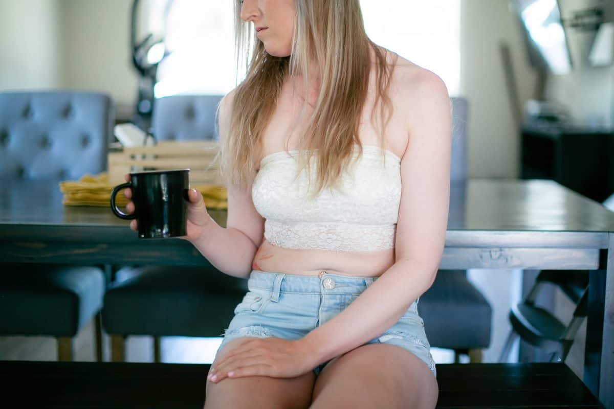 A white bandeau lace strapless bralette and denim shorts are worn by a woman holding a black mug