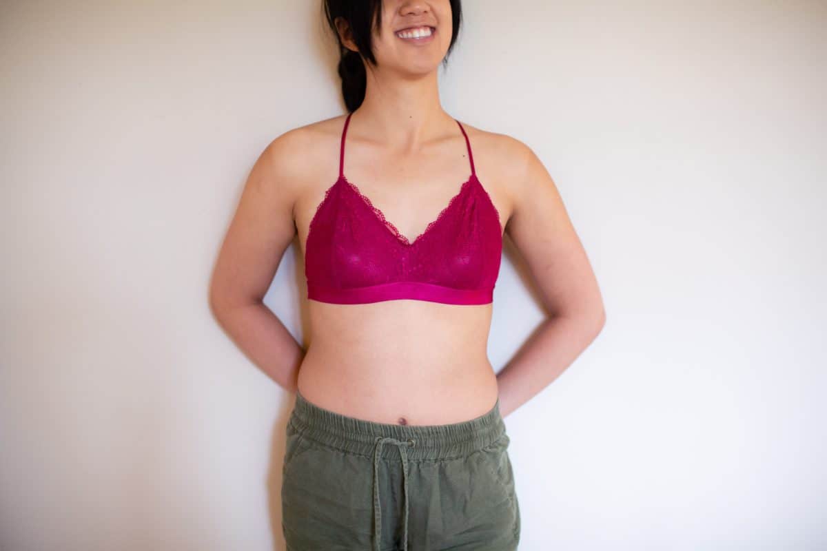 A woman wearing a pink racerback bralette and green shorts leaning on a white wall