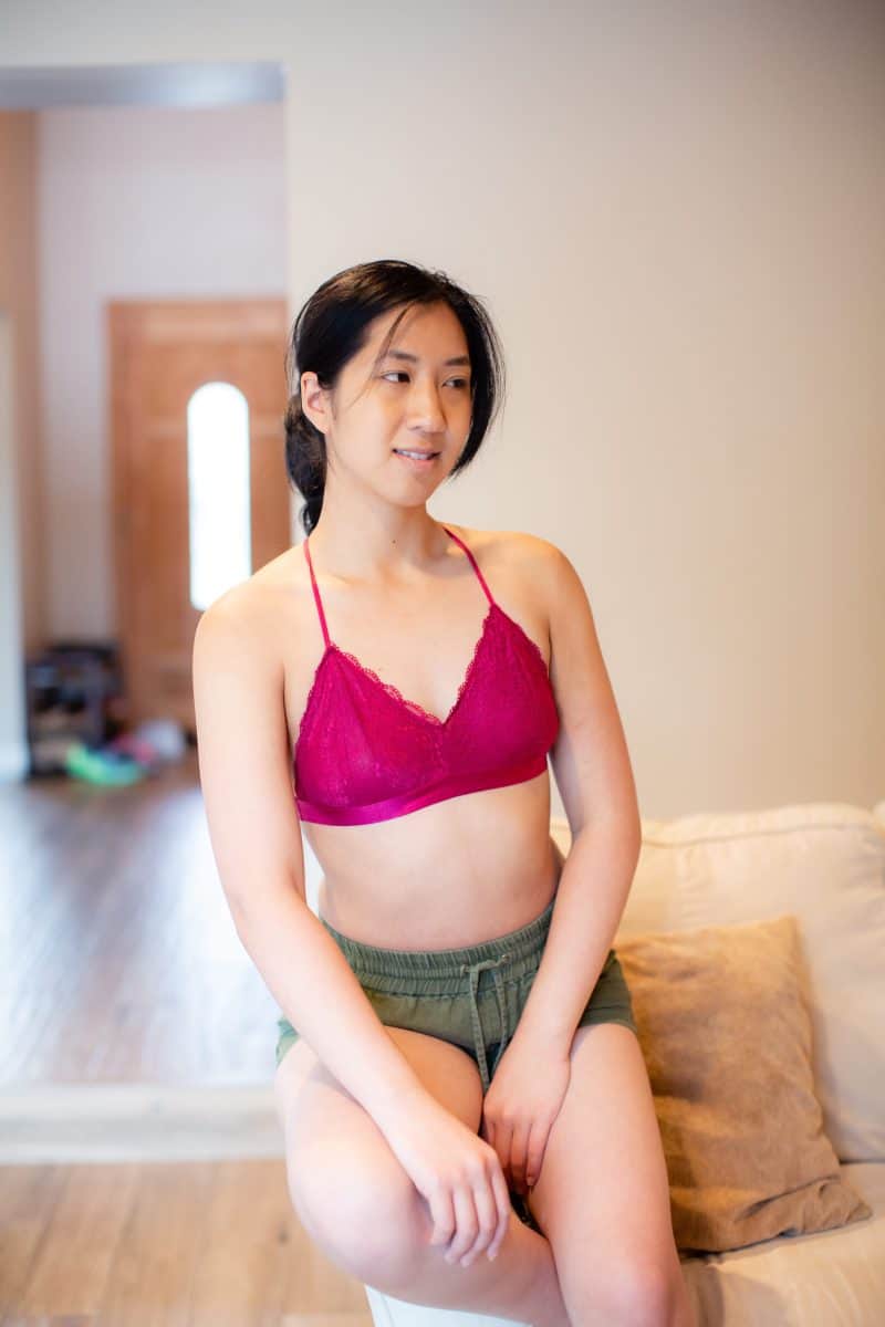 A young woman wearing a pink wireless bralette and green shorts is seated on a couch