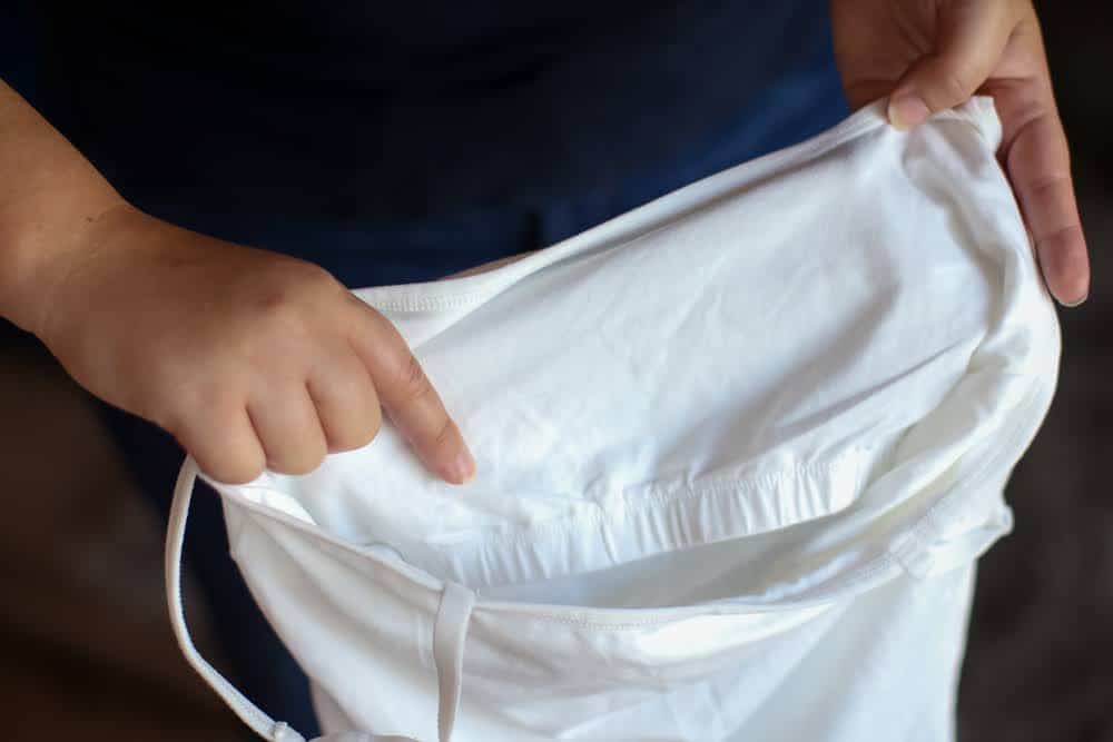 A white tank top with a built-in bra holds by a person in blue t-shirt
