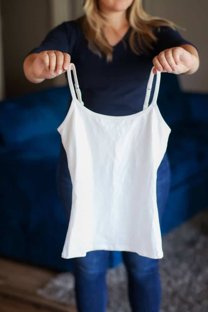 A woman in blue t-shirt and denim pants holds a white tank top