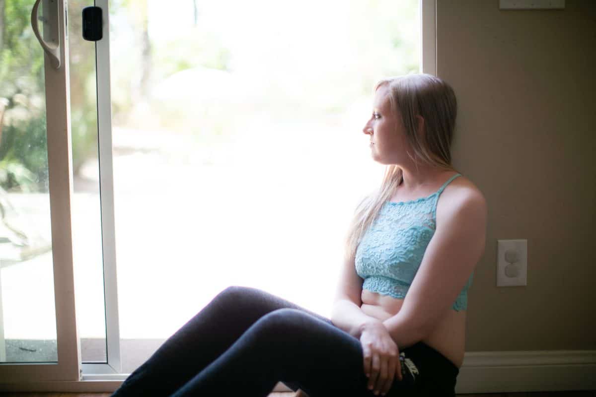 A blue lace high-neck bralette and black leggings are worn by a woman seated looking outside the window
