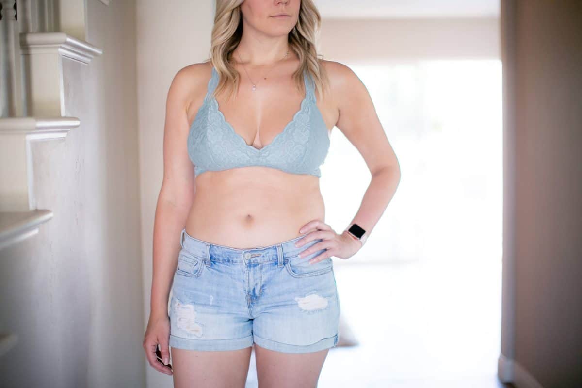 A woman wearing a blue lace bralette and denim shorts standing near a staircase