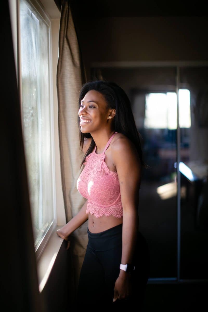 Pink high-neck halter bralette with underwire and black leggings worn by a woman looking at the window