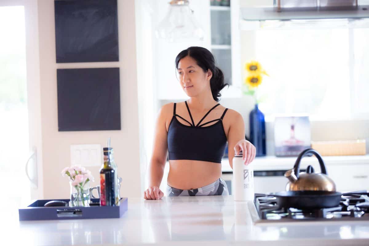 A blue high-neck halter bralette and colorful leggings are worn by a woman standing in the kitchen