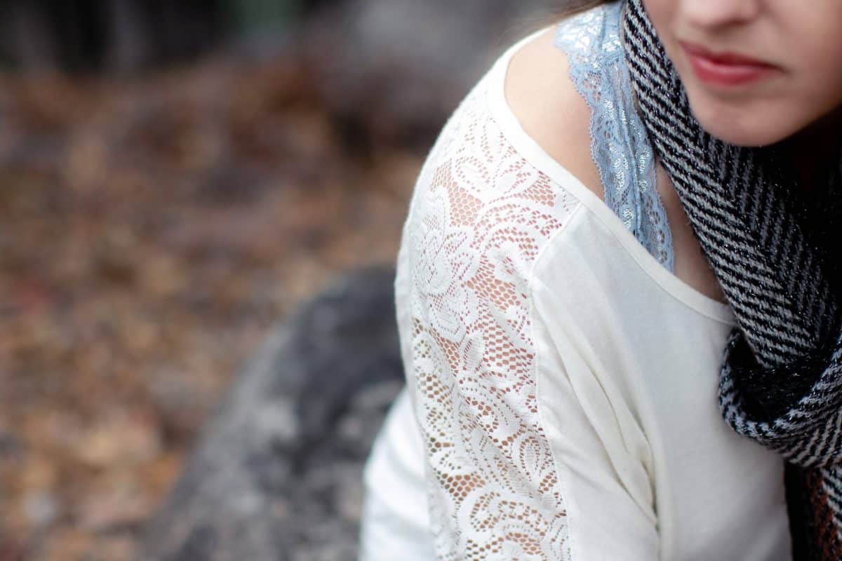 A blue lace bralette and white blouse were worn by a woman seated on the rock