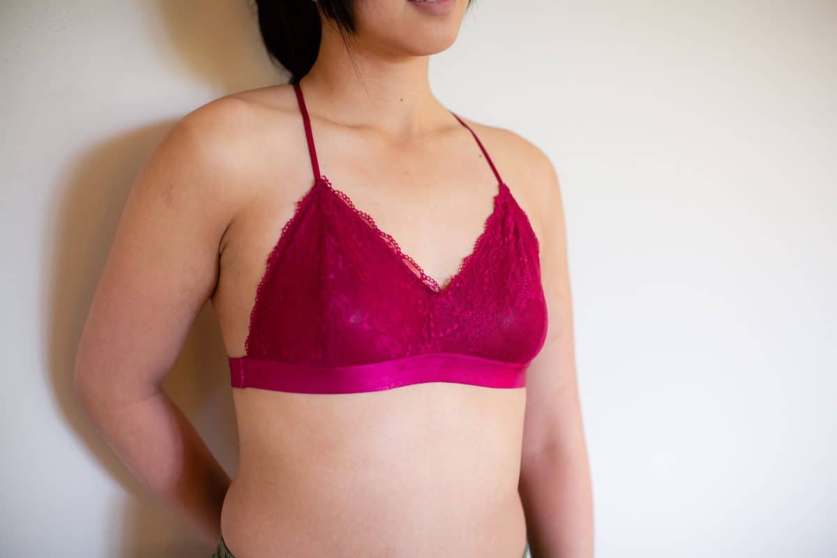 A woman leaning on the wall wearing a pink lace bralette