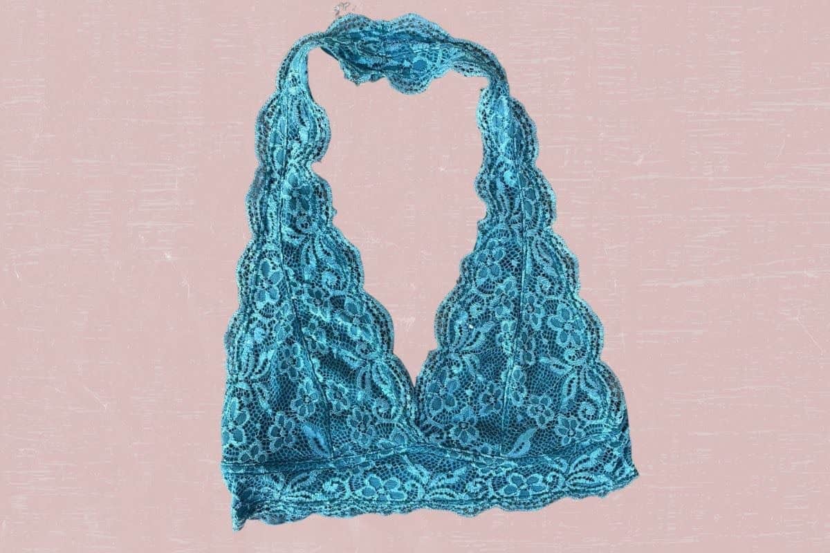A blue lace halter bralette with a floral design placed on a pink background