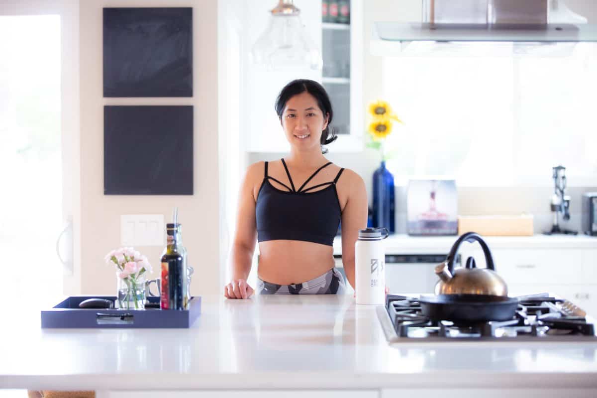 A woman wearing a dark blue high-neck bralette and leggings standing in the kitchen