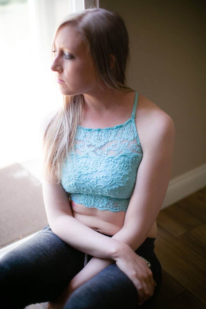 A woman wearing a blue high-neck lace longline bralette and jogging pants seated on the floor