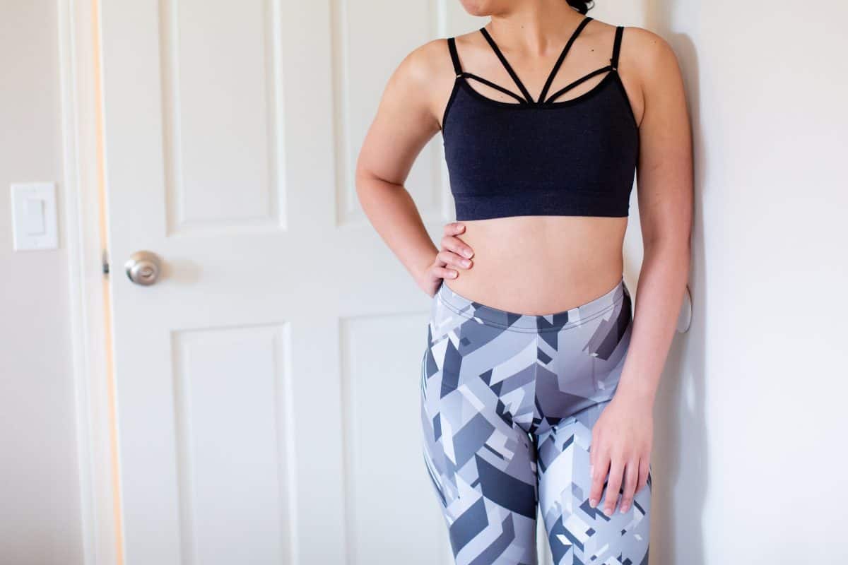A dark blue high-neck bralette and leggings are worn by a woman leaning on a white wall