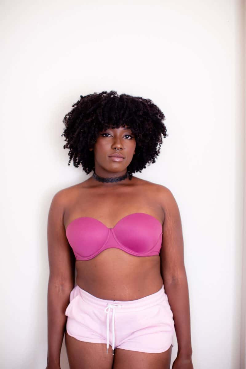 Woman wearing a pink underwire strapless bra and pink shorts standing near a white wall