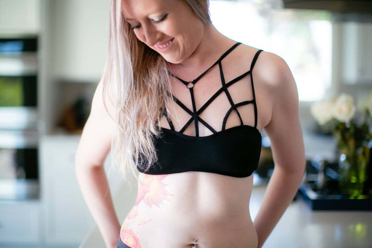A woman smiling and wearing a black cage bra standing in the kitchen