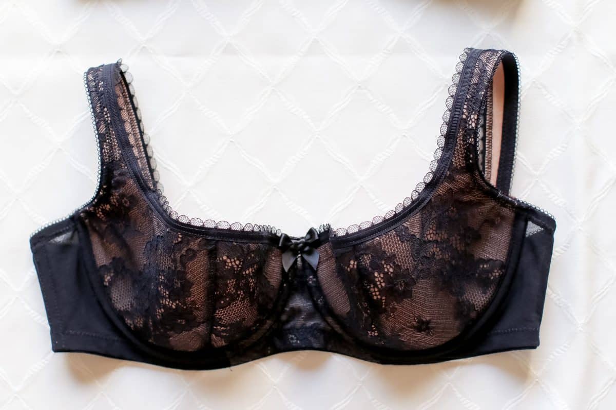A black underwire demi bra with a lace floral design placed on a white surface