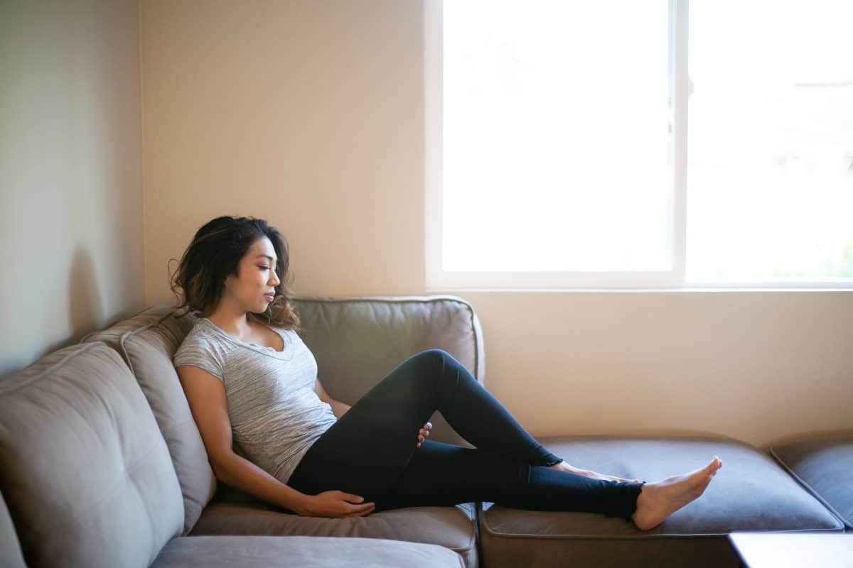 A gray v-neck shirt and black leggings are worn by a woman seated on a couch