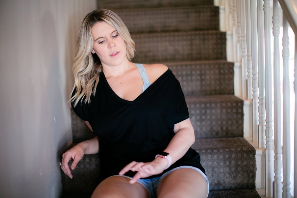 A black v-neck blouse and denim shorts are worn by a woman seated on the stairs
