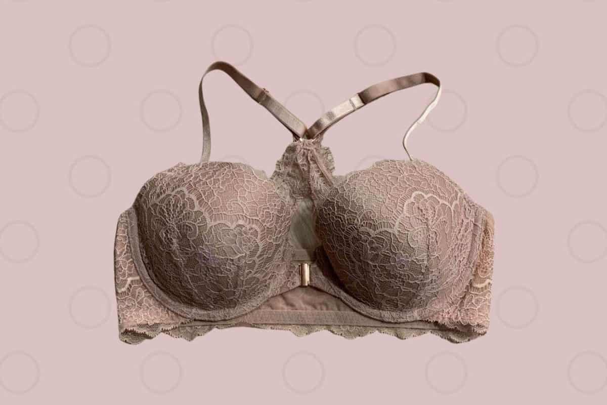 A nude racerback underwire bra with a lace design and front clasp placed on a pink background