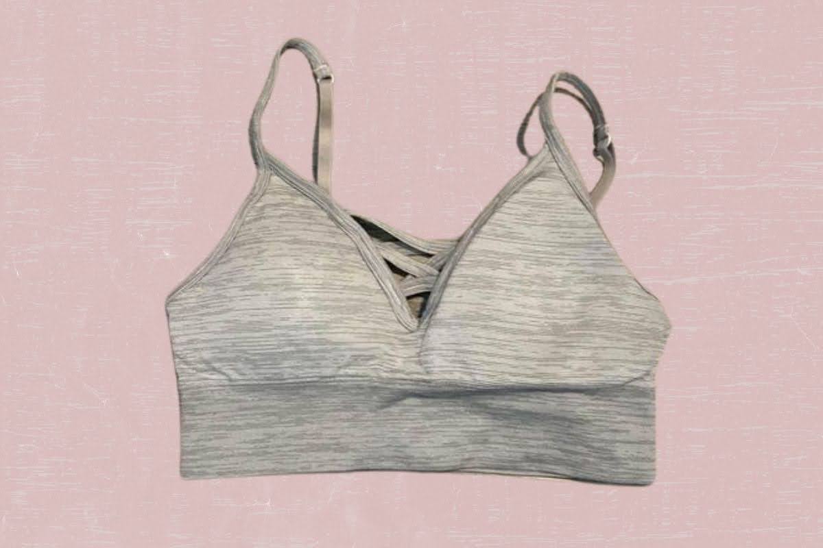A gray v-neck spaghetti strap sports bra placed on a pink background