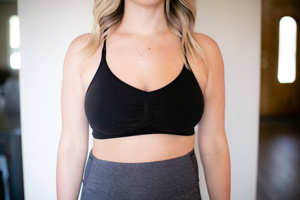 A black sports bra and gray leggings are worn by a woman standing near a white wall
